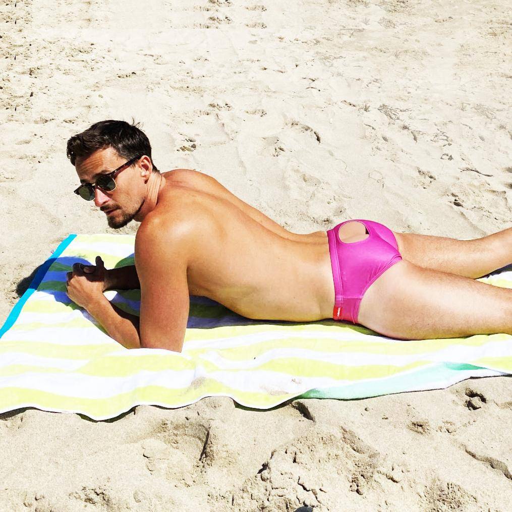 Man wearing pink swim brief on beach towel